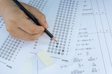 Students hand holding pencil writing selected choice on answer sheets and Mathematics question sheets. students testing doing examination. school exam