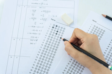 Obraz premium Students hand holding pencil writing selected choice on answer sheets and Mathematics question sheets. students testing doing examination. school exam
