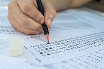 Students hand holding pencil writing selected choice on answer sheets and Mathematics question sheets. students testing doing examination. school exam