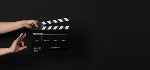 Hand is holding Black clapper board or movie slate on black background.Other hand do A ok or okay sign.