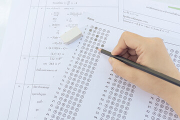 Obraz premium Students hand holding pencil writing selected choice on answer sheets and Mathematics question sheets. students testing doing examination. school exam