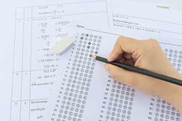 Obraz premium Students hand holding pencil writing selected choice on answer sheets and Mathematics question sheets. students testing doing examination. school exam