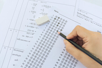 Obraz premium Students hand holding pencil writing selected choice on answer sheets and Mathematics question sheets. students testing doing examination. school exam