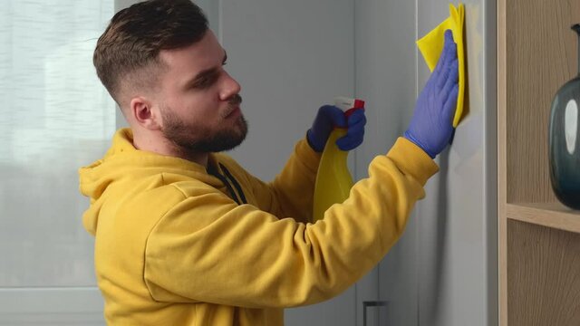 Bearded mam is cleaning the house using gloves and special disinfecting spray