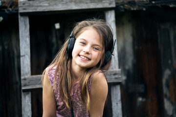 Obraz premium Happy little girl with headphones on the wooden stairs.