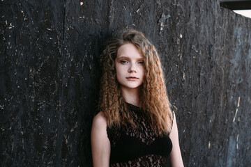 Fototapeta premium Red-haired girl in a black dress near a dark textured wall
