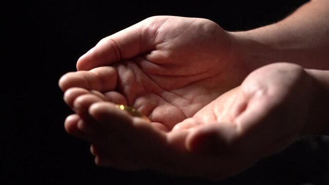 Pour Gold Coins on the Palm of the Man's Hands. Hands with gold coins on black background. Slow Motion