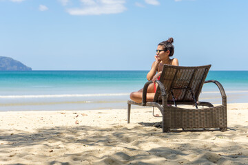 Woman on a beach, sitting in a deck chair and watching the sea