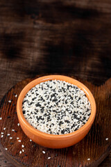 White and black sesame seeds in a ceramic bowl on a brown wooden table