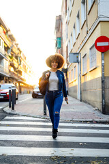 Black woman with afro hair crossing the street with a backpack in hand