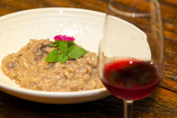 Risotto with chopped pork on wooden table with glass of red wine in the background.