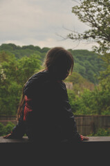 The girl is sitting on the windowsill. Turning around looks. Silhouette. Summer