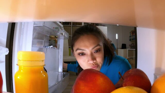 Young woman searches for food and drinks in the fridge - videoclip