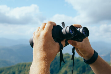 Hands holding binoculars on mountains forest nature background, looking through binoculars, travel,...