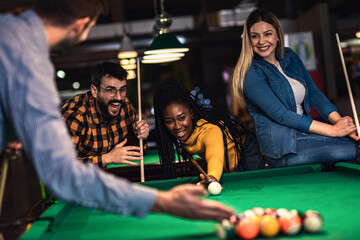 Four smiling friends in bar playing billiard together.