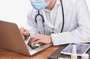 Physician typing on a laptop, giving an online consultation to a patient