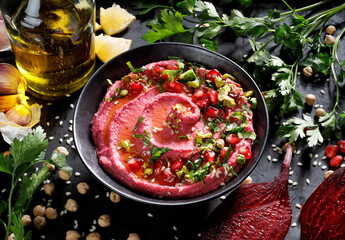 Beetroot hummus with olive oil sprinkled with fresh parsley, pomegranate seeds and pistachios in a black ceramic bowl, close up view