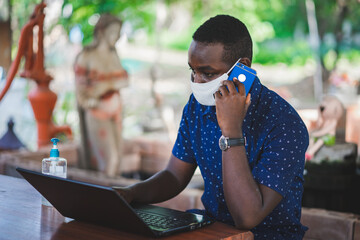 African man wearing a mask and using a laptop at home . WHF or Work from home concept