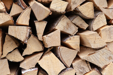 Background from a stack of firewood for heating a house, stacked in the backyard, uncut wood, birch. Concept for eco-friendly home heating during the cold season. Overall plan. Horizontal