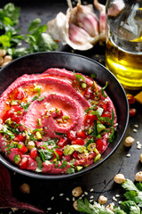Beetroot hummus with olive oil sprinkled with fresh parsley, pomegranate seeds and pistachios in a black ceramic bowl, close-up