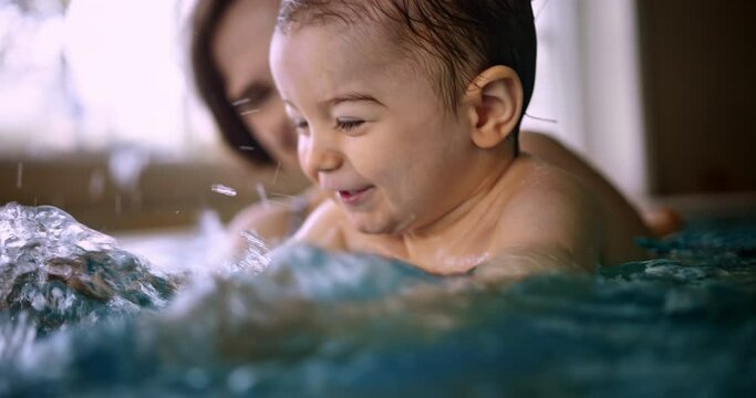 Happy baby splashing water playing with mom in indoor pool