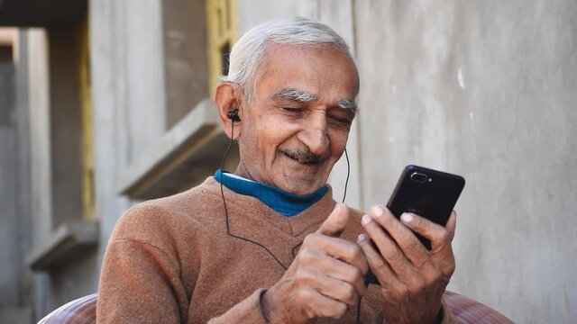 Bhuj, Gujarat, India - Circa 2020 : Portrait of happy old Indian man talking on videocall with family with vivid expressions. Concept of modern lifestyle of elder people with help of technology