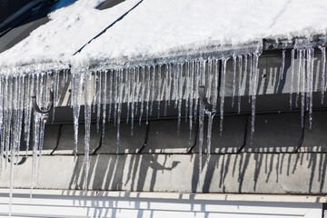 Eiszapfen an der Dachrinne eines Hauses tauen in der Wintersonne, Unfallgefahr.