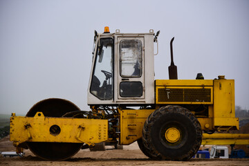 Old asphalt paver stands on the sand of a road under construction
