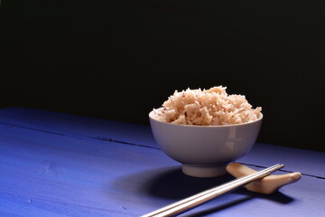 white rice in a bowl and chopsticks blue table on a dark green background with copy space