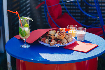 A glass of cocktail and a plate with a snack on the table. Kebab stick. Party food. Relax in a street cafe