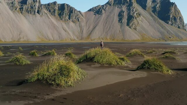 Epic drone view of the landscape in Stokksnes. Woman tourist on dune looking to the Vestrahorn mountain. Iceland nature.