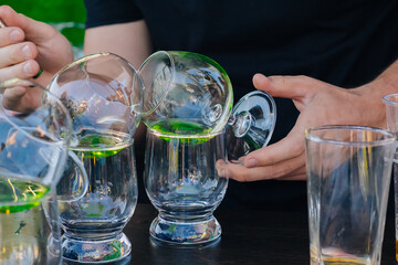 The bartender pours green absinthe into beautiful wine glasses and sets them on fire at a street party.