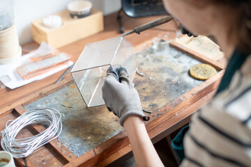 The girl works with a soldering iron in the workshop, connecting parts of the glass with foil and makes a cloche cap for decorative use.