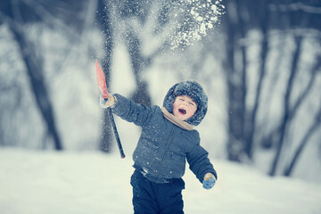 Cute laughing little boy throwing snow with a little red toy shovel. Image with selective focus and...