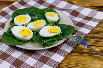 Boiled eggs with fresh spinach leaves and sesame seeds on wooden table