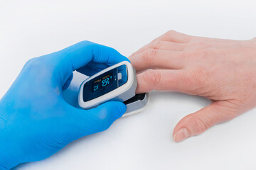 The doctor's hand in a latex medical glove holds a device to measure oxygen in the blood, pulsexymeter with the finger of an elderly woman on a white background