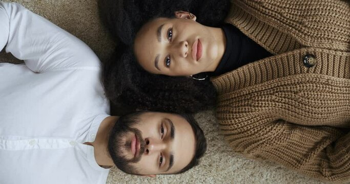 Young multiethnic couple afro american woman and caucasian man teenagers in love lying on floor after work day trying to relieve stress and relax sleep wake up open eyes look at the camera top view