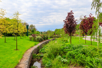 Beautiful view of the city park with arched footbridge across small river and young trees