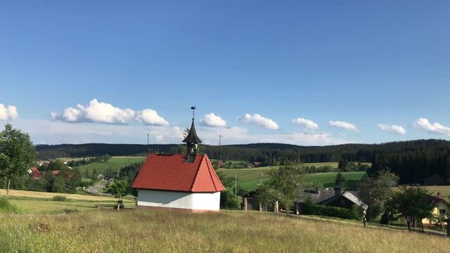 Small chapel in the Black Forest of Germany surrounded by golden fields. Green meadows and forest is in the background.