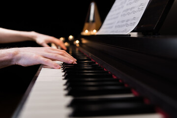 Hands playing the piano keyboard closeup and candle light bokeh background. Male pianist learning to play the piano instrument and beautiful music. Reading sheet music with metronome - Powered by Adobe