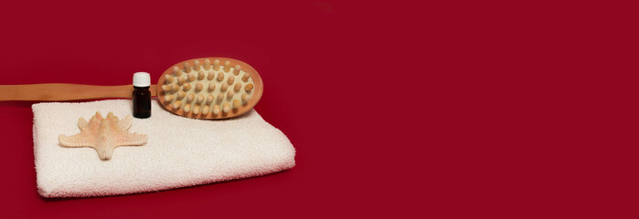 spa. starfish, anti-cellulite massage brush and essential oil on white towel, red background banner business