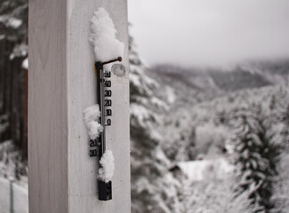 Retro Thermomenter mit Schneehaube an kaltem Wintertag vor winterlichem Wald 