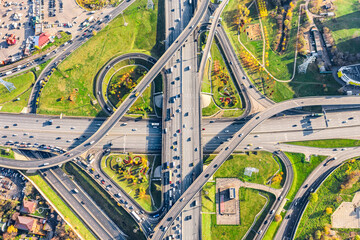 Aerial drone view of road interchange or highway intersection with busy urban traffic in modern city during sunny day. Traffic jam aerial view.