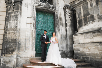 Wedding photo shooting. Bride and bridegroom walking in the city. Married couple embracing and looking at each other. Holding bouquet