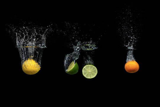 Fresh Citrus Fruit Falling Into The Water Isolated On A Black Background.