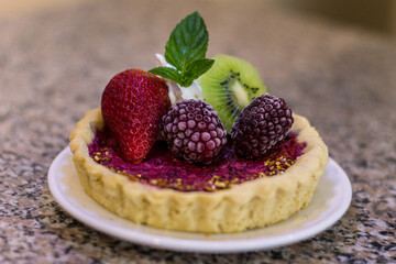 Postre, pie de frutos rojos con decoración de kiwi, fresa, mora, crema y menta.