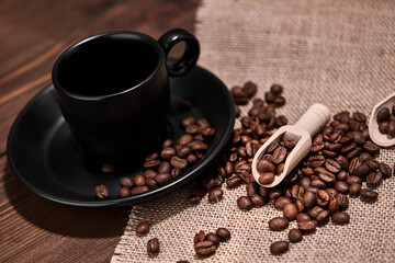 Close up of a cup of hot drink a wooden ladle with roasted coffee beans on a wooden kitchen table on a woven burlap with copy space to decorate the text