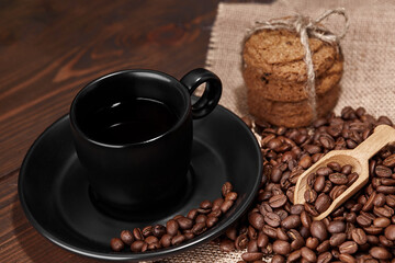 A cup of hot drink on roasted coffee beans and oatmeal cookies on a wooden kitchen table on woven burlap with copy space to decorate the text