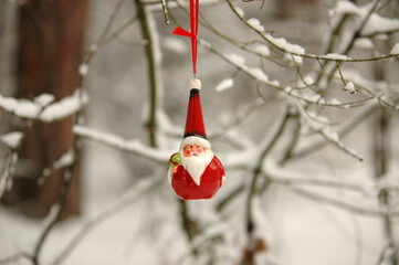 Red Santa Claus ornament in scandinavian style hanging on the tree in the winter forest