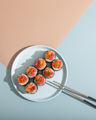 Japanese sushi roll on minimalistic blue and beige background with metal chopsticks top view isolated